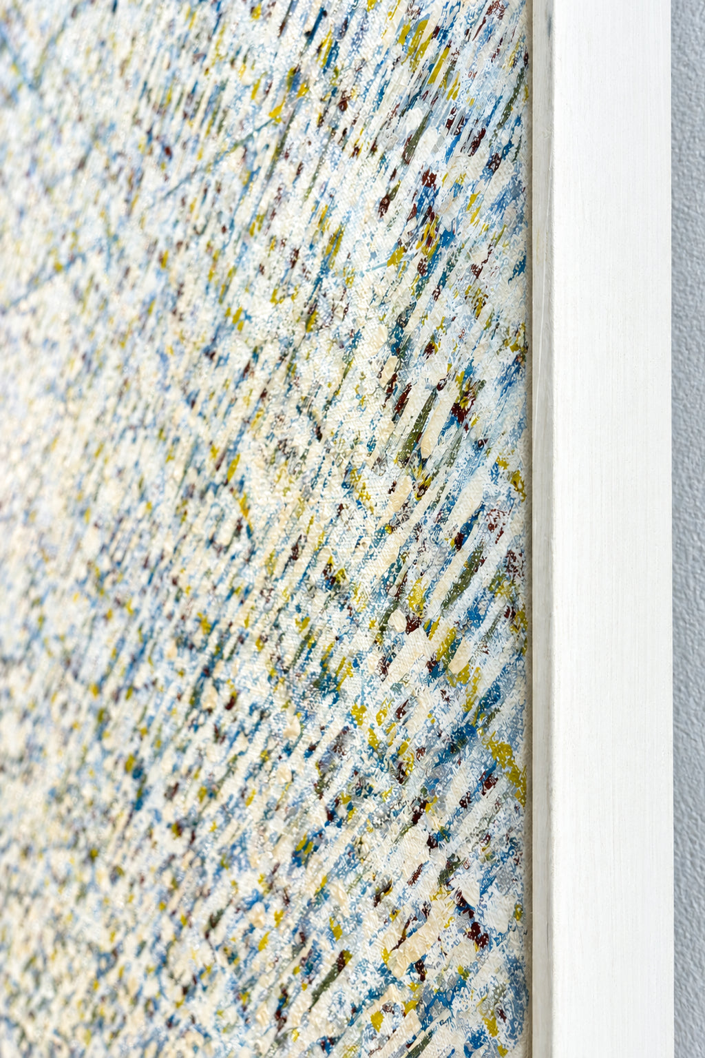 Close-up of a framed textile or rug sample with a textured abstract pattern in beige, blue, gray, and small yellow accents, shown next to a white frame edge.