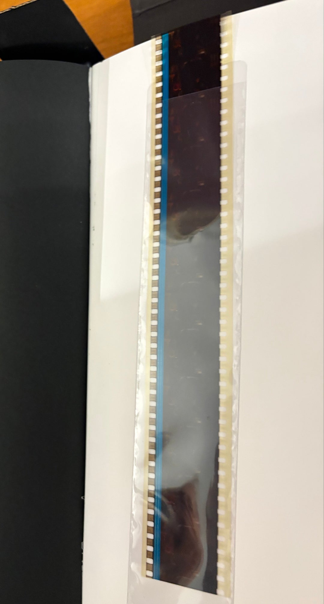 A close-up of a black book or album cover with a vertical translucent strip showing a dark printed design and small blue and cream details along the edge.