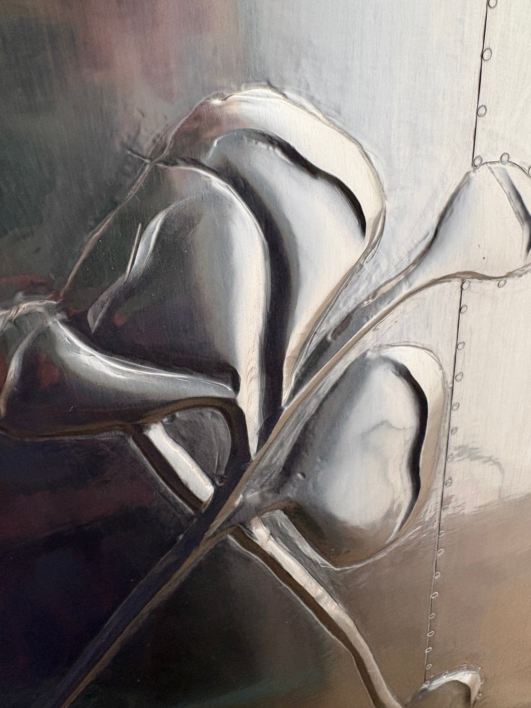 Close-up of a metallic silver surface with raised, glossy abstract leaf-like or organic raised details and a brushed metal background.