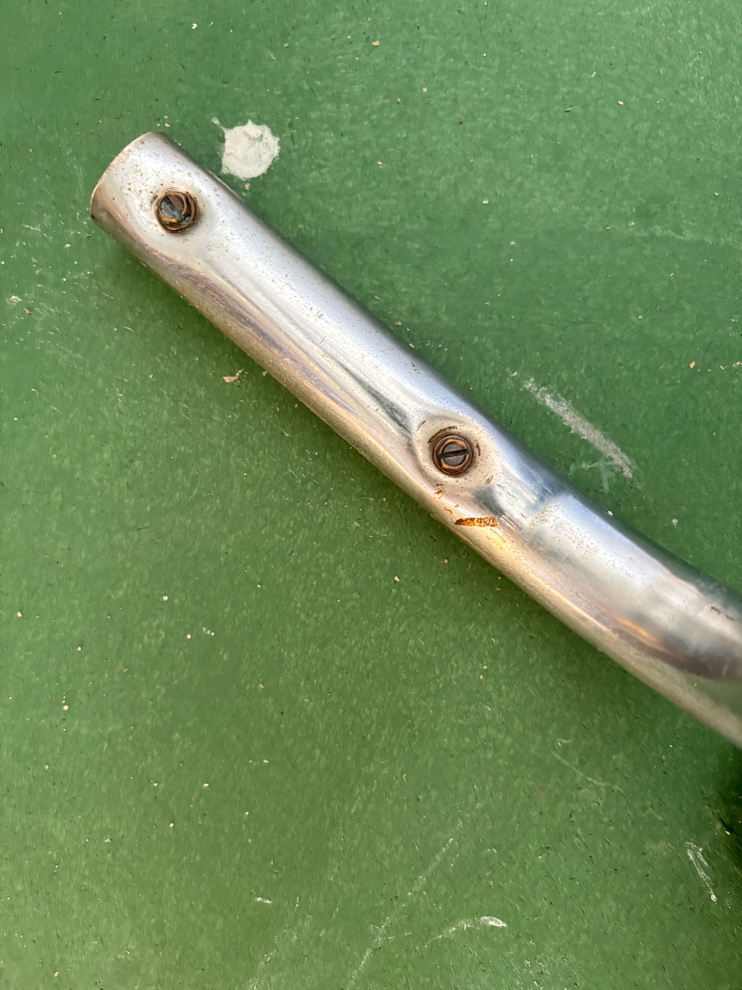 A close-up of a metallic silver cylindrical component with two visible screws, placed diagonally on a textured green surface.
