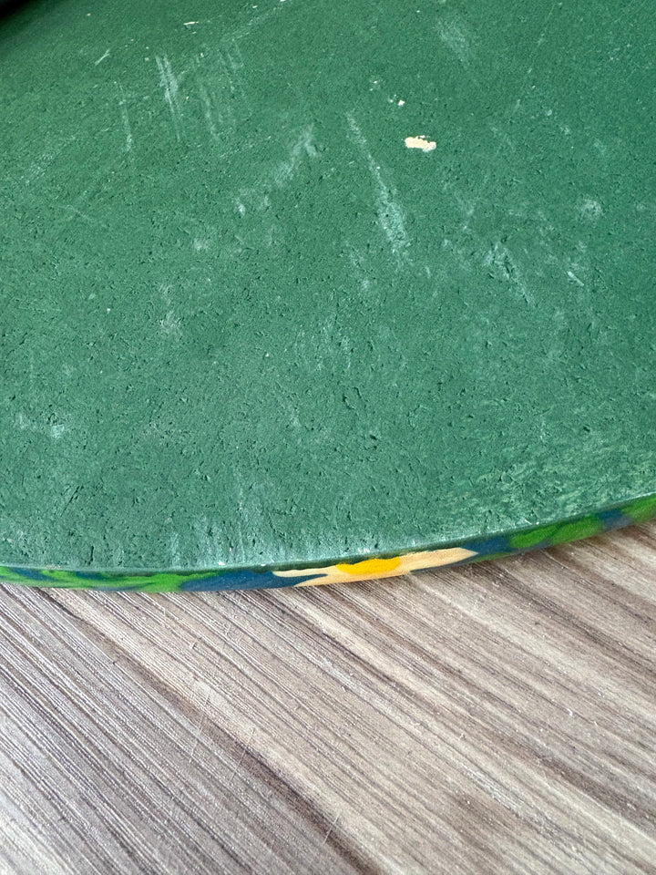 A close-up of a green textured surface, likely a protective mat or pad, showing some scuffs and scratches, positioned next to a gray wood-grain surface.