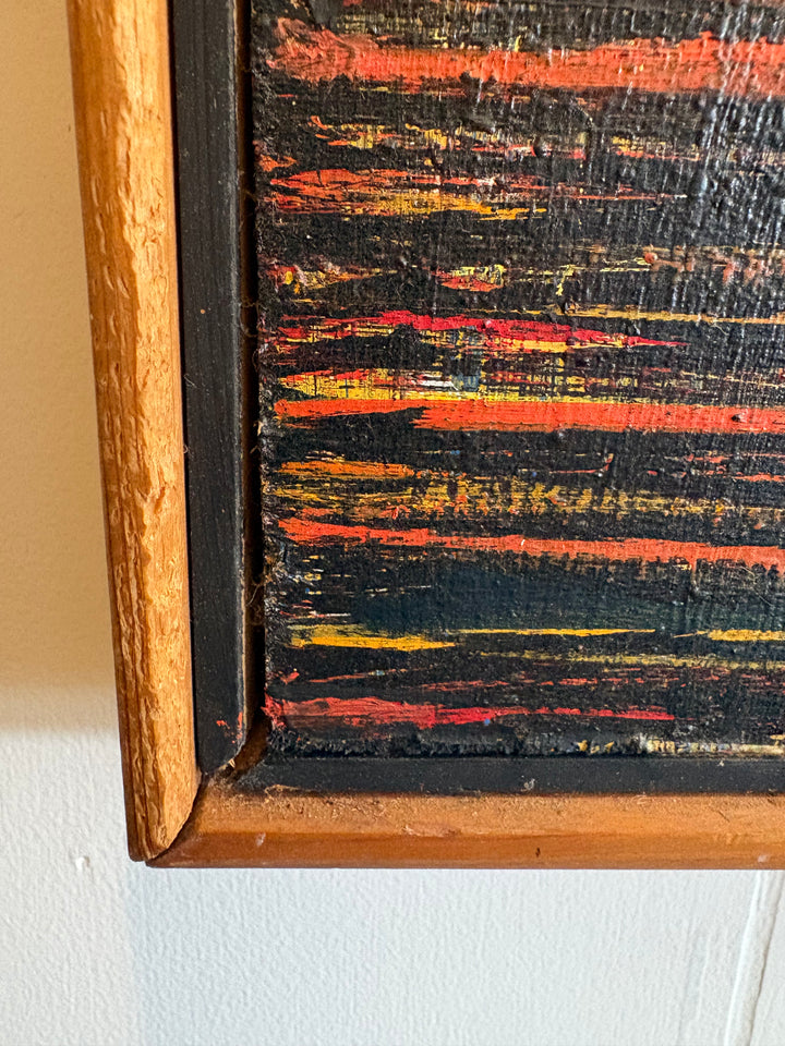 Close-up of a framed abstract painting showing textured horizontal brushstrokes in black, red, orange, and yellow, with a light wood frame against a white wall.