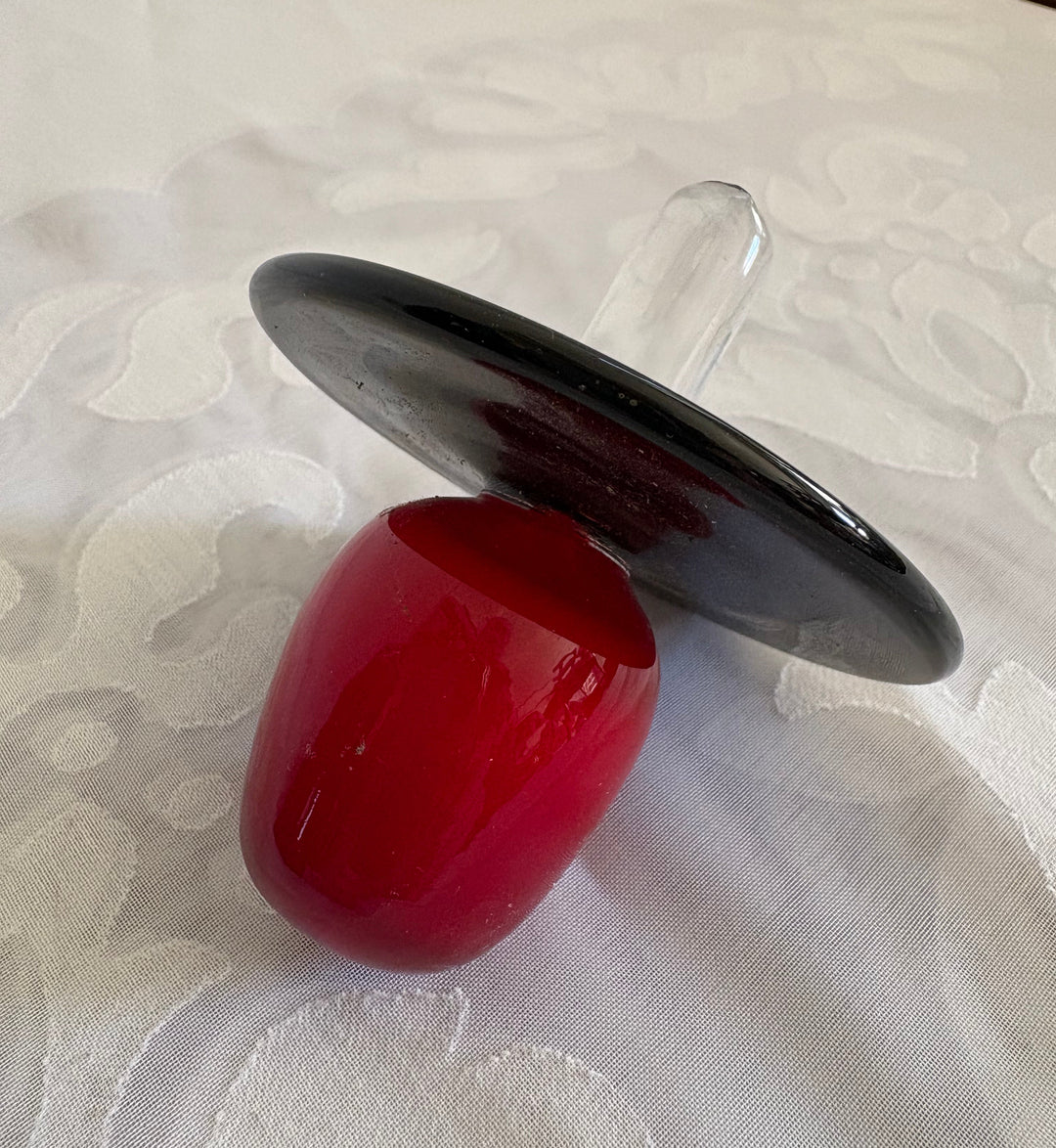 A murano glass red and black decanter top with a clear stem, resting on a white textured fabric background.