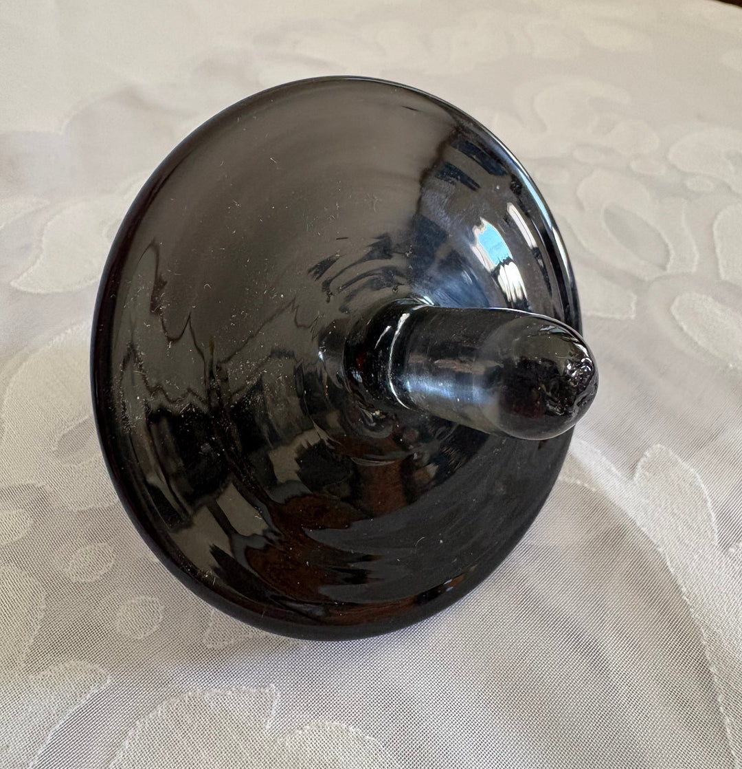 A glossy black glass decanter topper, resting on a white textured fabric surface.