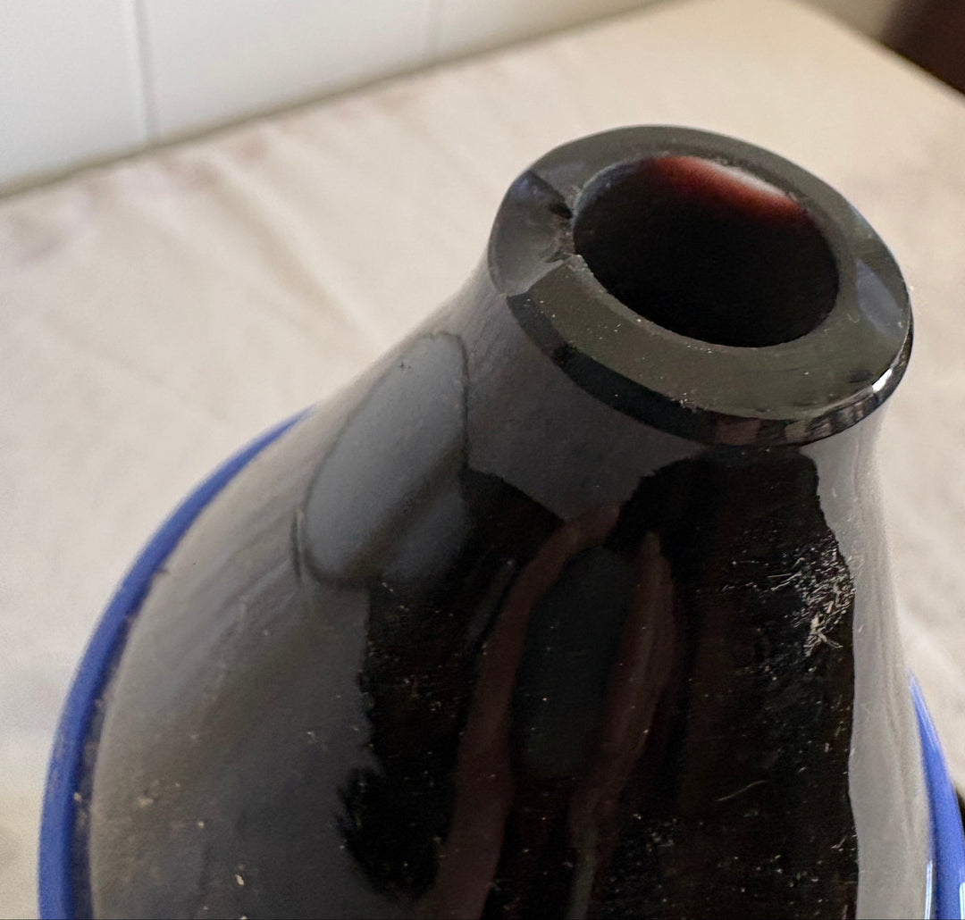 Close-up of a black Murano Glass decanter with a flared rim, resting on a white fabric surface. There is a chip on the lip.