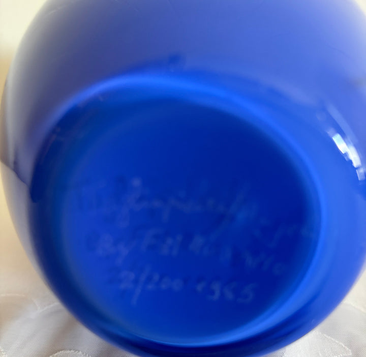 A close-up of the bottom of a cobalt blue glass decanter showing embossed handwritten markings, resting on a white textured fabric surface.